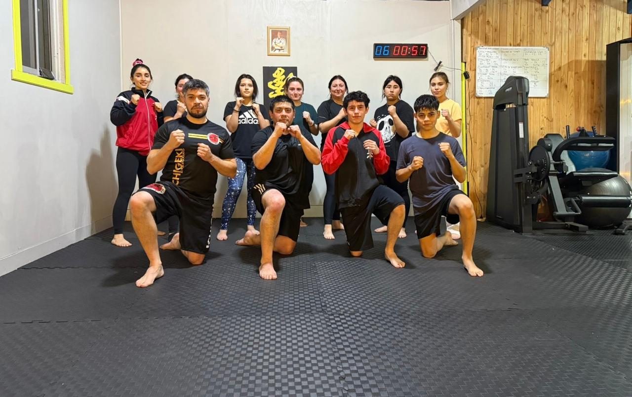 Grupo de Kickboxing Ichigeki en posición baja durante un entrenamiento, con la camiseta ICHIGEKI y el temporizador al fondo